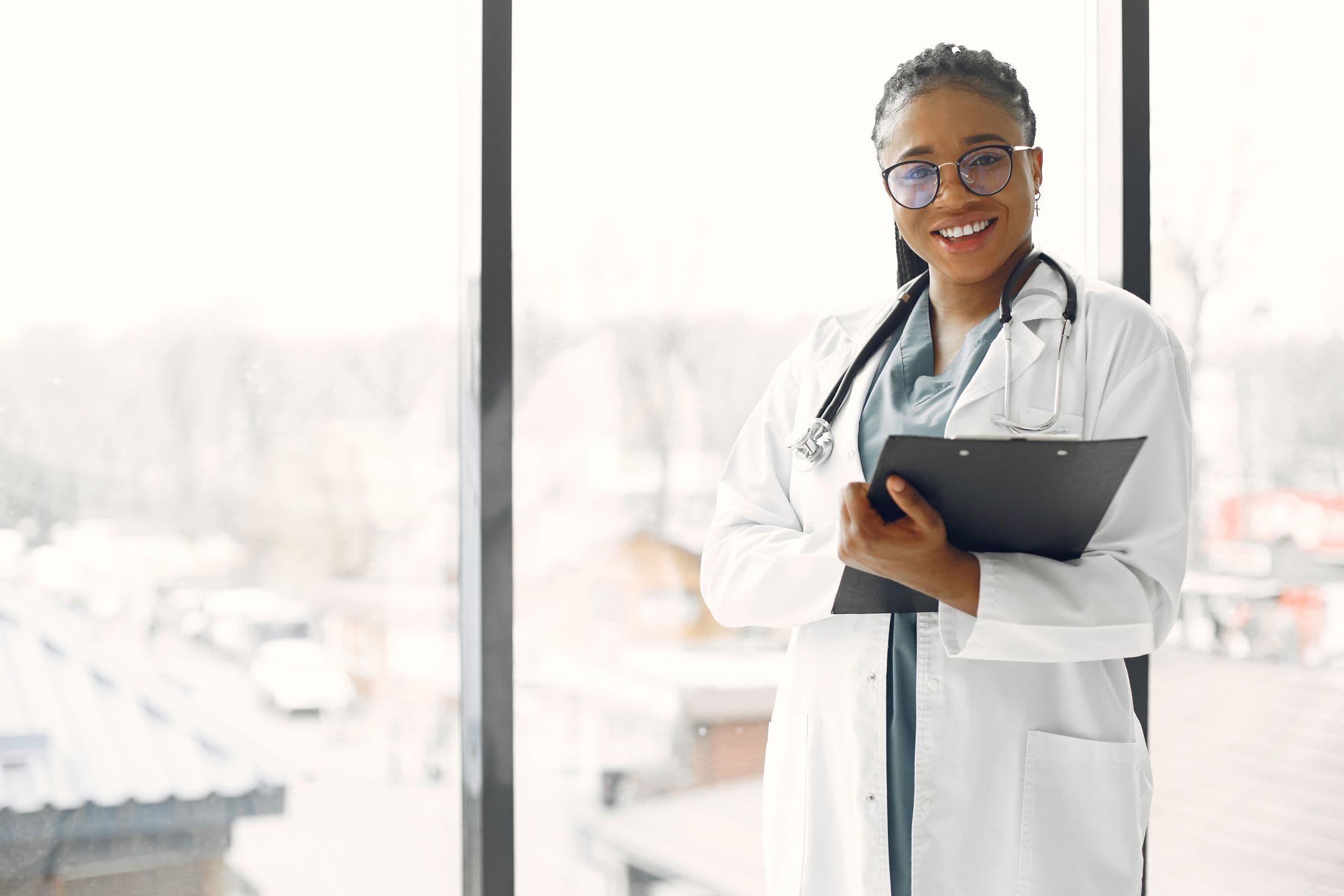 A doctor smiling warmly by a window — calm, soft natural light, ready to care